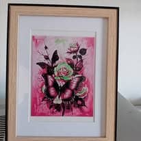 Tableau sous cadre en bois clair avec passe-partout blanc, représentant un grand papillon posé sur des roses, dans des tons rose fuchsia et vert.