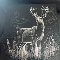 Plaque murale en relief représentant un grand cerf aux bois déployés, debout dans les hautes herbes d'un sous-bois, en blanc sur fond sombre.