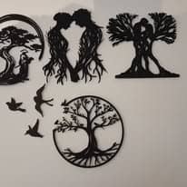 Ensemble de décorations murales noires ajourées posées sur un mur clair : arbre de vie circulaire, couples d'arbres enlacés et oiseaux en vol.