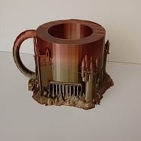Mug imprimé en 3D en dégradé cuivré, dont la base est sculptée en muraille de château avec une herse et des tours.